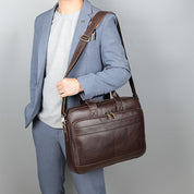 Uomo in abito blu con borsa a tracolla in pelle marrone, elegante e professionale, ideale per lavoro e ufficio. Accessorio moda maschile.