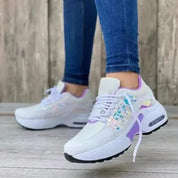 Scarpe da ginnastica bianche e viola con dettagli iridescenti, indossate da una persona con jeans aderenti. Sneakers moda donna, stile casual.