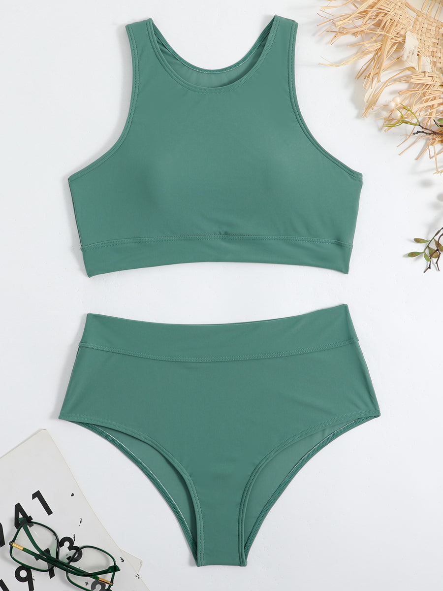 Costume da bagno verde a due pezzi, top sportivo e slip a vita alta, su sfondo bianco con occhiali e accessori estivi. Moda mare donna.