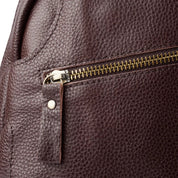 Zaino in pelle marrone con texture granulosa, cerniera in metallo dorato e tiralampo in pelle. Accessorio moda elegante e resistente.