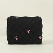 Borsa nera trapuntata con cerniera, decorata con fiocchi rosa. Accessorio moda elegante, ideale per organizzare oggetti personali.