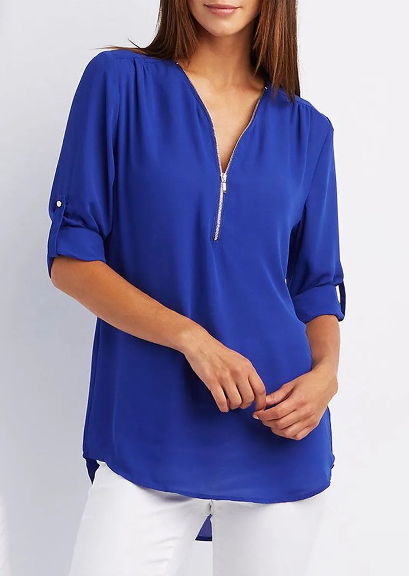 Blusa donna blu elettrico con zip frontale, maniche a 3/4 arrotolate, abbinata a pantaloni bianchi. Moda casual elegante, tessuto leggero.