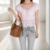 Donna con top rosa a balze e jeans grigi, tiene una borsa a spalla marrone in pelle. Moda casual femminile, abbigliamento estivo elegante.