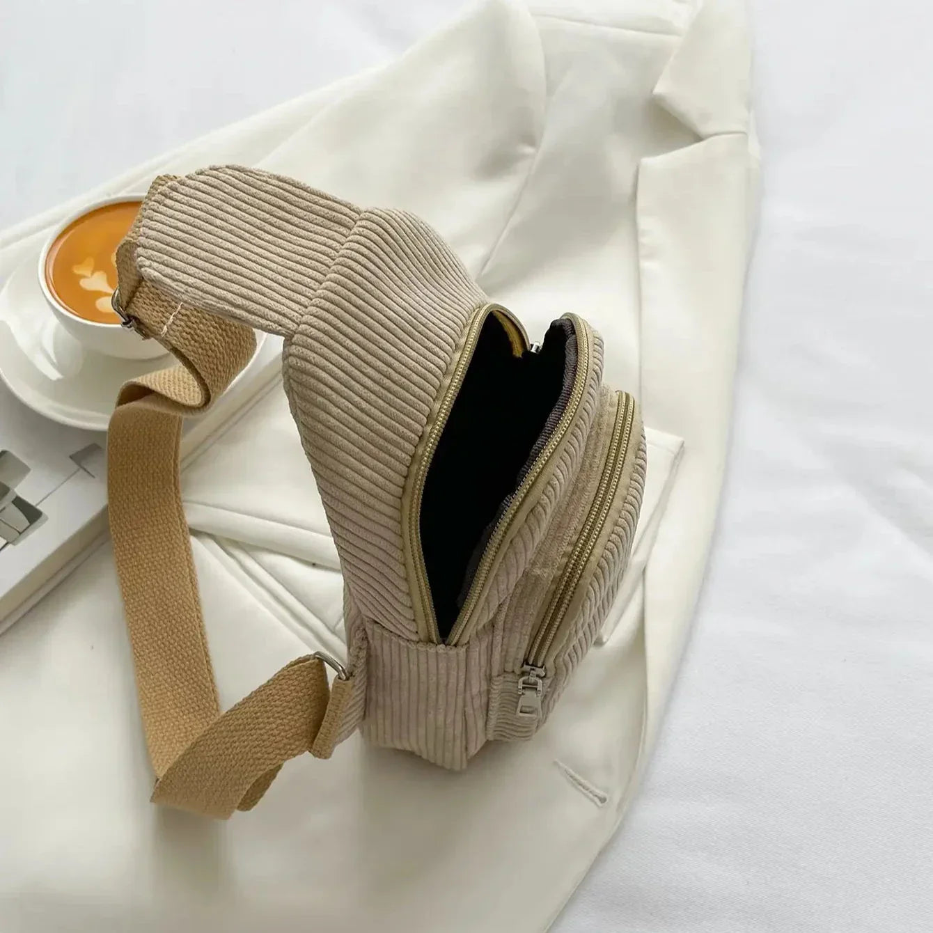 Marsupio beige a coste su giacca bianca, con caffè accanto. Design elegante, ideale per moda casual e viaggi. Accessorio pratico e di tendenza.