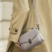 Cappotto beige con borsa a tracolla in pelle grigia, design elegante, chiusura a scatto, moda autunnale, accessorio di tendenza per donna.