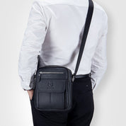 Uomo con borsa a tracolla in pelle nera, elegante e pratica, con zip e tasche multiple. Ideale per lavoro e viaggi. Accessorio moda maschile.