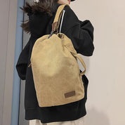Zaino in tela beige su persona con cappotto nero, design minimalista, ideale per scuola o viaggio. Accessorio moda unisex, resistente e spazioso.
