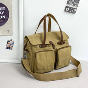 Borsa a tracolla in tela beige con manici in pelle marrone, tasche frontali con zip, ideale per viaggi e uso quotidiano. Design elegante e funzionale.