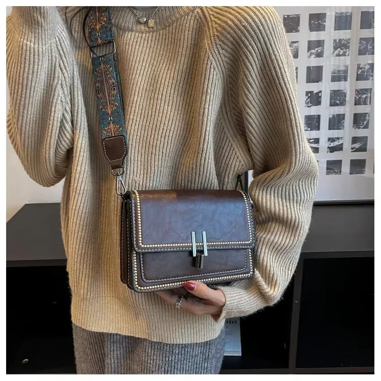 Donna con maglione beige indossa borsa a tracolla marrone in pelle con chiusura metallica, tracolla decorata. Elegante accessorio moda autunno.