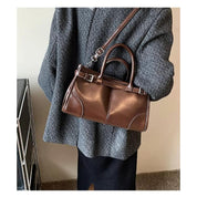 Borsa a mano in pelle marrone con tracolla, indossata su cappotto grigio. Elegante accessorio moda donna, stile autunno inverno.