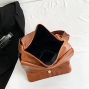 Borsa a tracolla in pelle marrone aperta su letto bianco, con tasca interna visibile. Elegante accessorio moda, ideale per lavoro e viaggio.