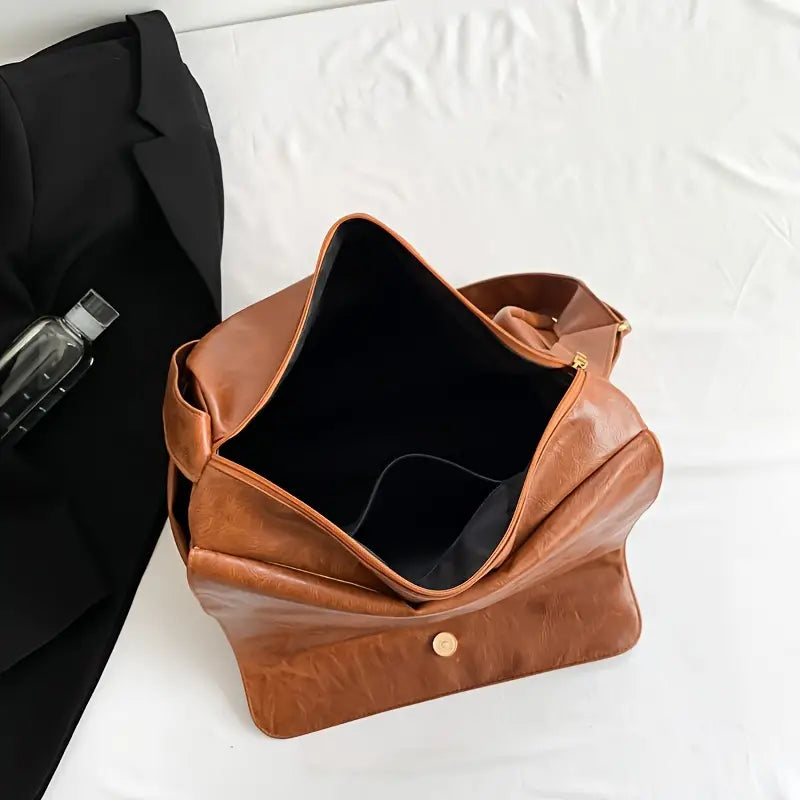 Borsa a tracolla in pelle marrone aperta su letto bianco, con tasca interna visibile. Elegante accessorio moda, ideale per lavoro e viaggio.