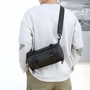 Zaino a tracolla nero unisex, indossato su maglia grigia. Design moderno, ideale per viaggi e uso quotidiano. Accessorio moda versatile.