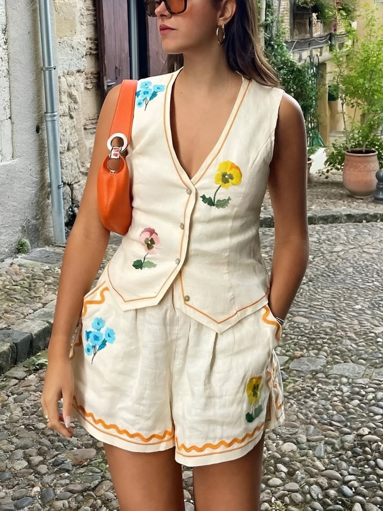 Donna con completo estivo in lino bianco, decorato con fiori colorati, borsa arancione, occhiali da sole, su strada acciottolata. Moda estiva casual.