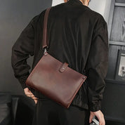 Borsa a tracolla in pelle marrone, indossata da una persona con giacca nera. Design elegante, ideale per moda urbana e accessori di tendenza.