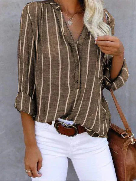 Camicia a righe verticali marrone e bianca, maniche lunghe, abbinata a pantaloni bianchi e borsa marrone. Stile casual elegante per donna.