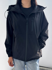 Giacca a vento nera da uomo con cappuccio, chiusura a zip, tasche laterali, indossata su jeans chiari. Abbigliamento casual, moda autunnale.