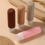 Quattro flaconi da viaggio in silicone colorati su sfondo beige, ideali per cosmetici e liquidi. Design compatto e riutilizzabile.