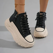 Scarpe da ginnastica alte nere e bianche con suola spessa, lacci e cerniera laterale, indossate su pavimento grigio. Moda calzature trendy.