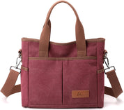 Borsa a tracolla in tela rosa con manici marroni, tasche frontali e tracolla regolabile. Design elegante e pratico per uso quotidiano.