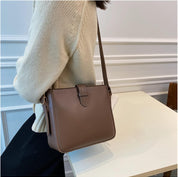 Borsa a tracolla marrone in pelle, design minimalista, indossata da una persona con maglione beige. Accessorio moda elegante per donna.