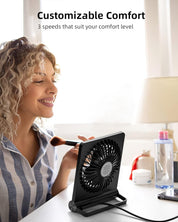 Donna sorridente usa ventilatore da tavolo nero con tre velocità, ideale per comfort personalizzato. Accessori trucco e bottiglia d'acqua sullo sfondo.