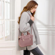 Donna con cappotto grigio e borsa a tracolla rosa, elegante e alla moda, in piedi vicino a una finestra. Accessori moda autunno inverno.