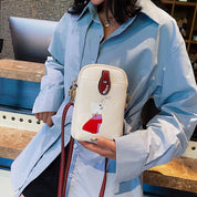 Donna con camicia azzurra tiene una borsa a tracolla bianca con stampa di gatto rosso. Accessorio moda, stile casual, tendenza 2023.