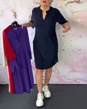 Donna in abito blu scuro con maniche corte, tiene abiti colorati su grucce. Sfondo decorativo rosa. Moda femminile, abbigliamento casual.