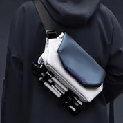 Zaino moderno e minimalista in tessuto tecnico blu e bianco, indossato su giacca scura. Design innovativo, ideale per moda urbana e viaggi.