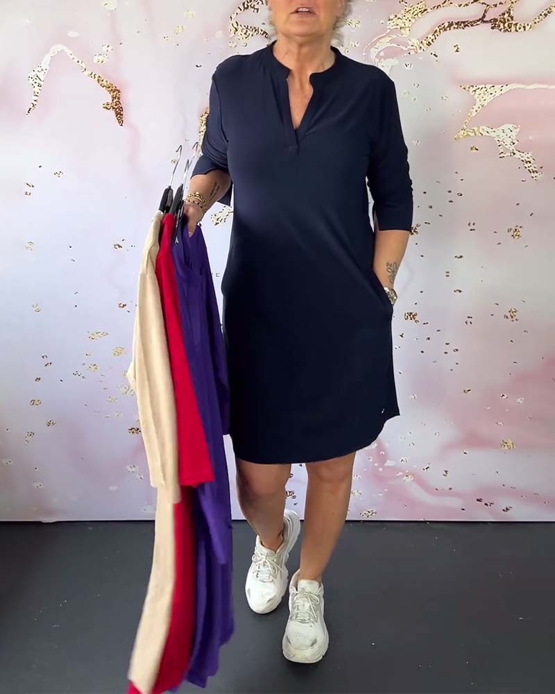 Donna con abito blu scuro, maniche a tre quarti, tiene abiti colorati su grucce. Sfondo decorativo rosa e bianco. Scarpe da ginnastica bianche.