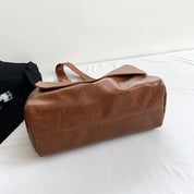 Borsa da viaggio in pelle marrone su letto bianco, design elegante e spazioso, ideale per viaggi e weekend. Accessorio moda uomo e donna.