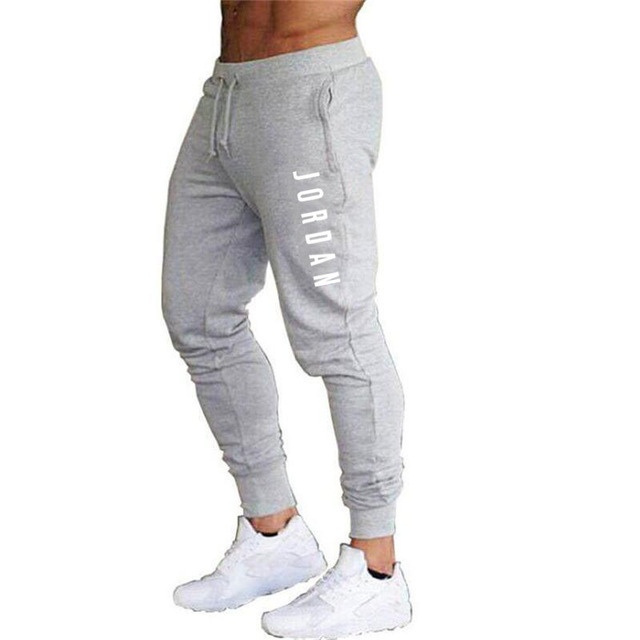 Pantaloni jogger grigi da uomo con scritta "Jordan", elastico in vita e caviglie, abbinati a scarpe sportive bianche.