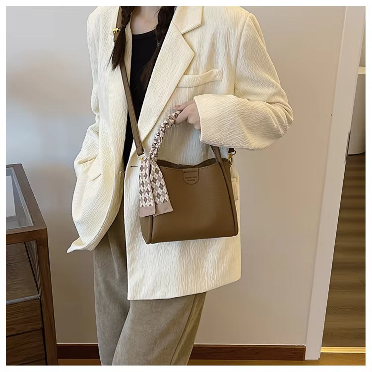 Donna con cappotto bianco e borsa a tracolla marrone, dettagliata con foulard. Moda autunnale, stile elegante, abbigliamento casual chic.