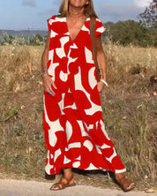 Abito lungo estivo rosso e bianco con motivo astratto, indossato da donna su strada di campagna. Stile casual, perfetto per giornate calde.