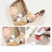 Borsa cosmetica beige aperta con scomparti, contenente flaconi di cosmetici, pennelli e accessori. Design impermeabile, ideale per viaggi e organizzazione.