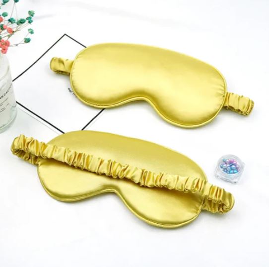Mascherine per dormire in seta dorata su sfondo bianco, con elastico arricciato. Accessori per il sonno, eleganti e confortevoli.