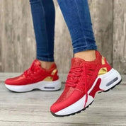 Scarpe da ginnastica rosse da donna con suola bianca e dettagli dorati, indossate con jeans. Design moderno, comode per sport e tempo libero.