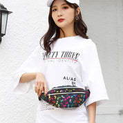 Donna con marsupio floreale, indossa t-shirt bianca e cappello. Moda casual, accessori colorati, street style. Sfondo bianco.