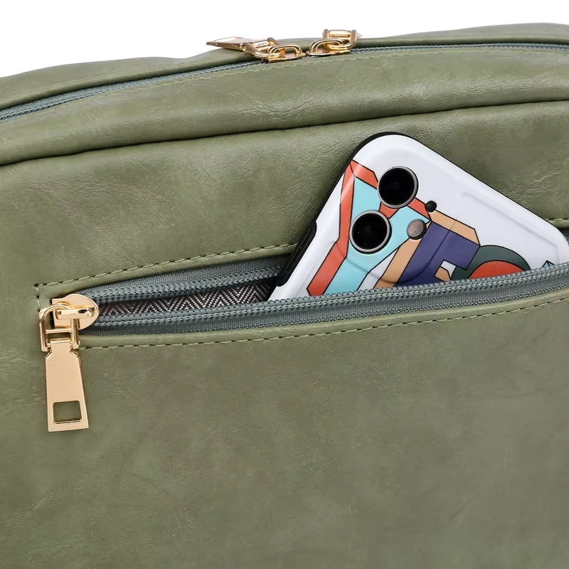 Zaino verde in pelle sintetica con tasca frontale, chiusura a zip dorata, contenente uno smartphone. Design moderno e funzionale.