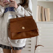 Donna con borsa a tracolla in pelle marrone, indossa felpa grigia. Accessorio moda elegante, perfetto per look casual e quotidiani.