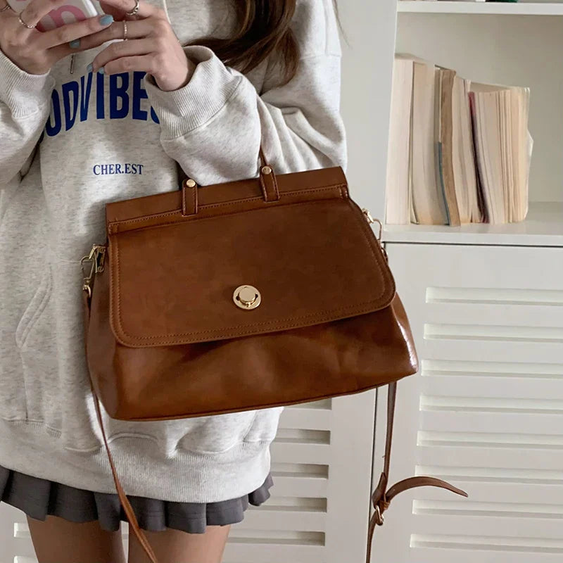 Donna con borsa a tracolla in pelle marrone, indossa felpa grigia. Accessorio moda elegante, perfetto per look casual e quotidiani.