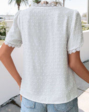 Maglietta bianca a pois con maniche corte e dettagli in pizzo, indossata da una persona all'aperto. Stile casual estivo, moda donna.