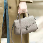 Borsa a mano in pelle grigia, design elegante, chiusura a scatto, tracolla regolabile, indossata con cappotto beige e jeans. Accessorio moda donna.