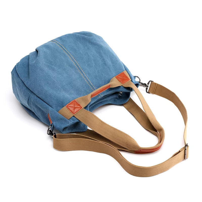 Zaino in tela blu con dettagli in pelle marrone, spallacci regolabili beige. Design casual, ideale per viaggi e uso quotidiano.