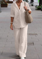 Donna con camicia bianca e pantaloni larghi, borsa intrecciata beige, cammina su marciapiede urbano. Moda casual elegante, abbigliamento estivo.