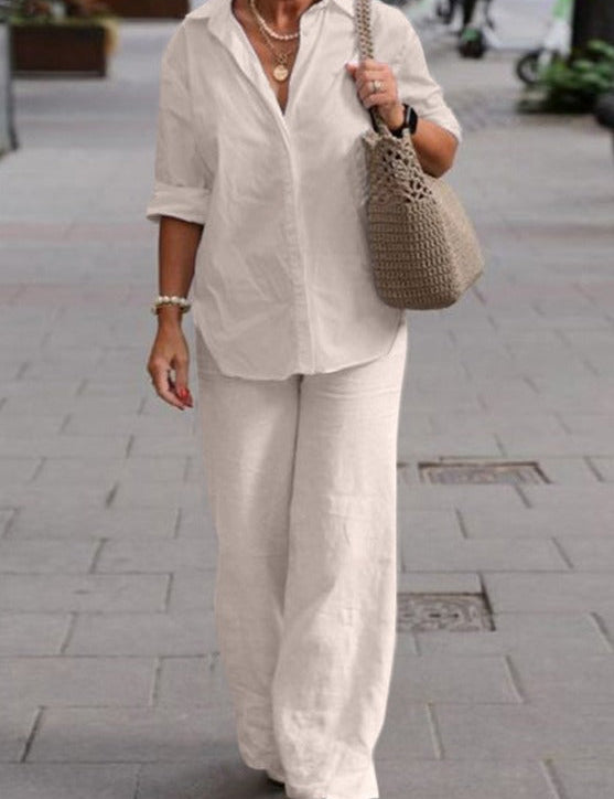 Donna con camicia bianca e pantaloni larghi, borsa intrecciata beige, cammina su marciapiede urbano. Moda casual elegante, abbigliamento estivo.