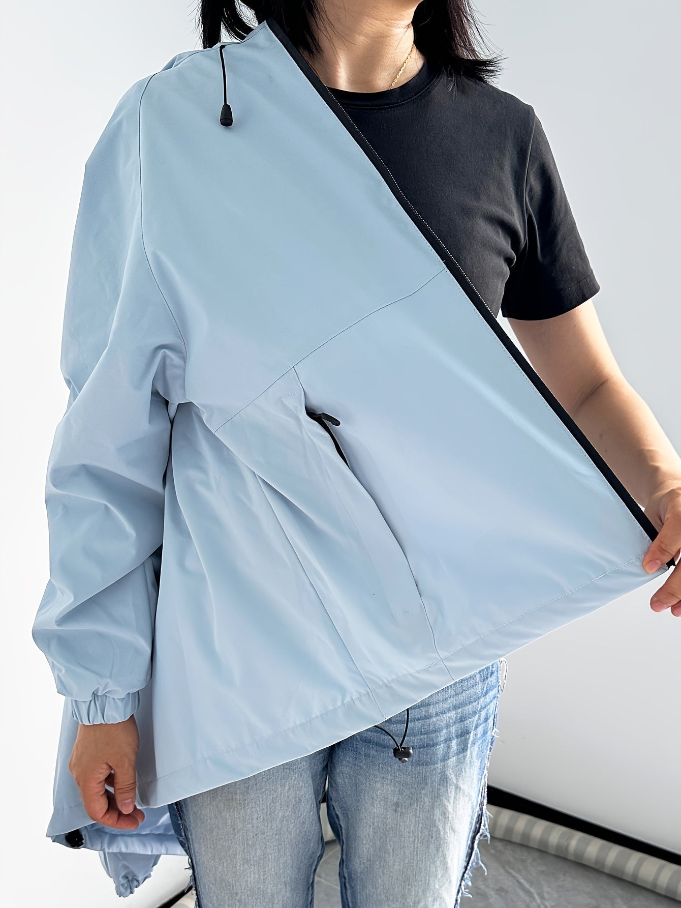 Giacca a vento azzurra unisex, indossata sopra una maglietta nera e jeans. Design moderno, ideale per moda casual e protezione dal vento.