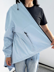 Giacca a vento azzurra unisex, indossata sopra una maglietta nera e jeans. Design moderno, ideale per moda casual e protezione dal vento.