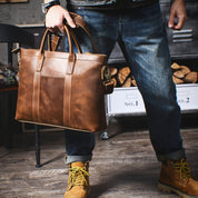 Borsa a mano in pelle marrone per uomo, elegante e resistente, indossata con jeans e stivali. Accessorio moda maschile di alta qualità.